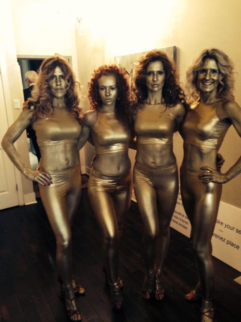Four women wearing gold pants and tops, and makeup